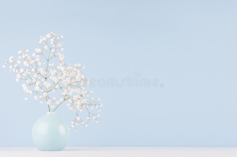 Ljus mjuk elegant hem- dekor med små luftiga blommor i glansig pastellfärgad blå vas på trätabellen och den blåa väggen royaltyfri fotografi Ljus mjuk elegant hem- dekor med små luftiga blommor i glansig pastellfärgad blå vas på trätabellen och den blåa väggen royaltyfri fotografi