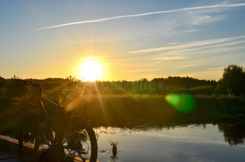 Ljus soluppgång på vägen nära floden på bakgrunden av en cykel Mountainbike i skog med solstrålar fotografering för bildbyråer Ljus soluppgång på vägen nära floden på bakgrunden av en cykel Mountainbike i skog med solstrålar fotografering för bildbyråer