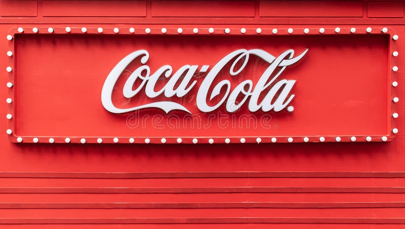 Ljusbox med logotyp coca cola på röd bakgrundsvägg arkivfoto