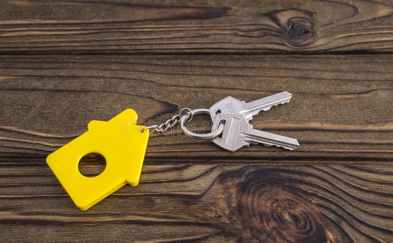Llave con llavero formado amarillo de la casa en cadena en el fondo de madera de la textura imagenes de archivo Llave con llavero formado amarillo de la casa en cadena en el fondo de madera de la textura imagenes de archivo