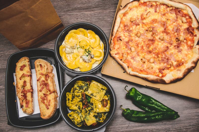 Llévese la comida italiana de las pastas Pizza con pimientas de verde de la caja, pan de ajo, fetuccine y los raviolis en la caja foto de archivo Llévese la comida italiana de las pastas Pizza con pimientas de verde de la caja, pan de ajo, fetuccine y los raviolis en la caja foto de archivo