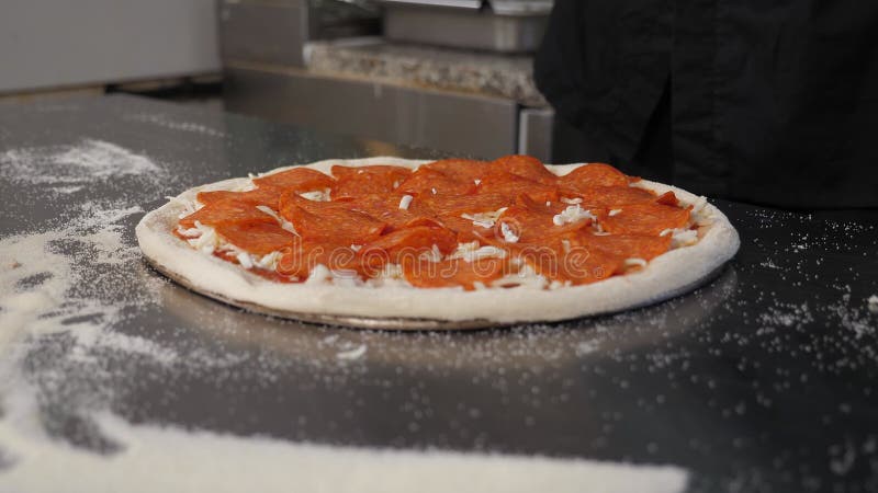 Lo chef spruzza la pizza salsiccia con formaggio grattugiato nella cucina pizzeria. stock footage