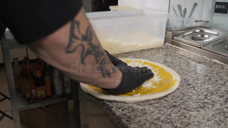 Lo chef versa formaggio grattugiato su pasta per pizza con salsa nella cucina del ristorante video d archivio