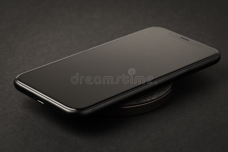 Lo smartphone è ricaricato da un caricatore wireless su uno sfondo nero Il concetto di nuove tecnologie fotografia stock Lo smartphone è ricaricato da un caricatore wireless su uno sfondo nero Il concetto di nuove tecnologie fotografia stock