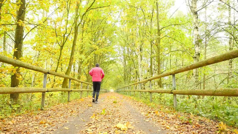 Lo sportivo in abiti sportivi rosa e neri funziona sulla strada L'uomo sta correndo lentamente sul modo dell'asfalto coperto dall