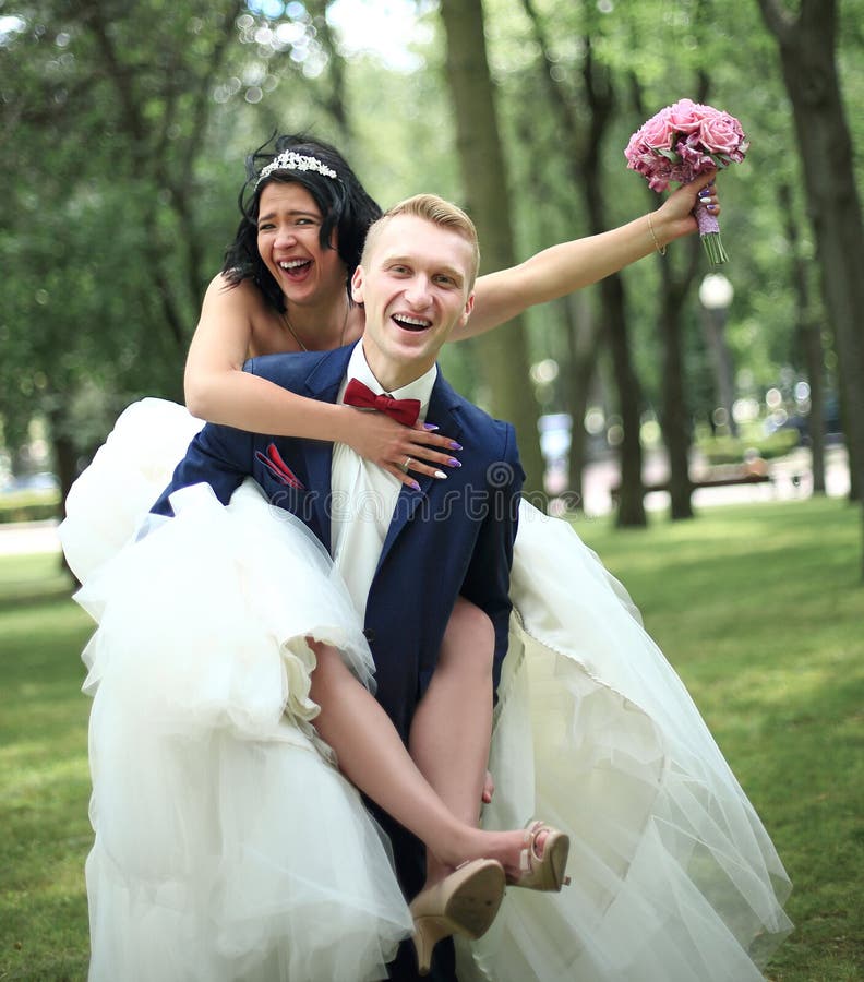 Lo sposo porta la sua sposa sulla parte posteriore nel parco immagini stock Lo sposo porta la sua sposa sulla parte posteriore nel parco immagini stock