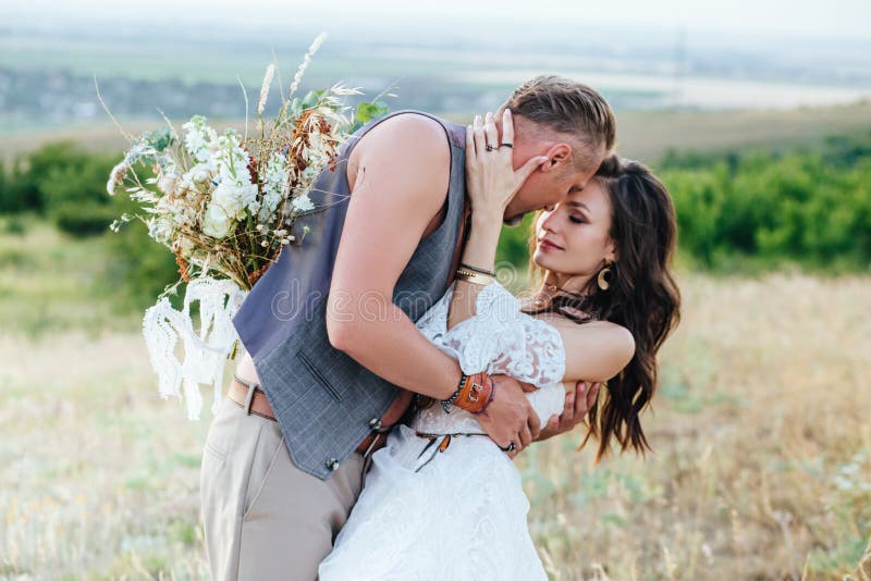 Lo sposo si è vestito nello stile del boho delicatamente bacia la sposa fotografia stock Lo sposo si è vestito nello stile del boho delicatamente bacia la sposa fotografia stock