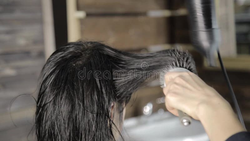 Lo stilista fa i capelli che disegnano per il bello cliente femminile ed il fon utilizzato con il pettine