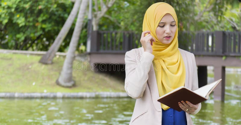 Lo studente di college grazioso gode di di leggere e ritenere nel parco immagini stock libere da diritti Lo studente di college grazioso gode di di leggere e ritenere nel parco immagini stock libere da diritti