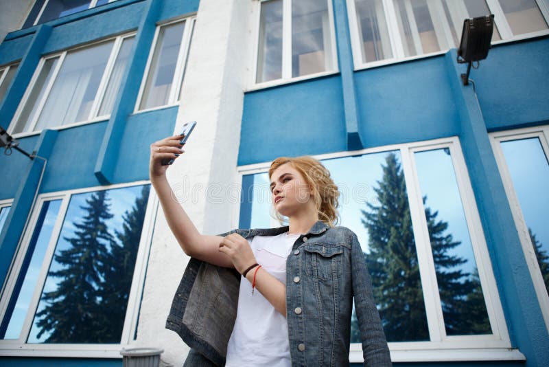 Lo studente fa un autoritratto con uno smartphone, bei pantaloni a vita bassa della ragazza che prendono le immagini se stessi co fotografia stock Lo studente fa un autoritratto con uno smartphone, bei pantaloni a vita bassa della ragazza che prendono le immagini se stessi co fotografia stock