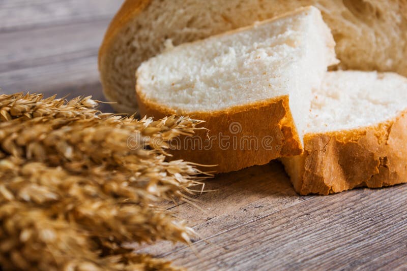 A loaf of bread and ears of ripe wheat lie on a wooden table stock photos