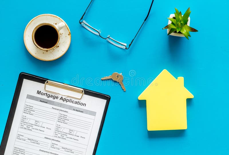 House mortgage with application, glasses, coffee, house toy, keys on blue banker desk background top view stock image House mortgage with application, glasses, coffee, house toy, keys on blue banker desk background top view stock image