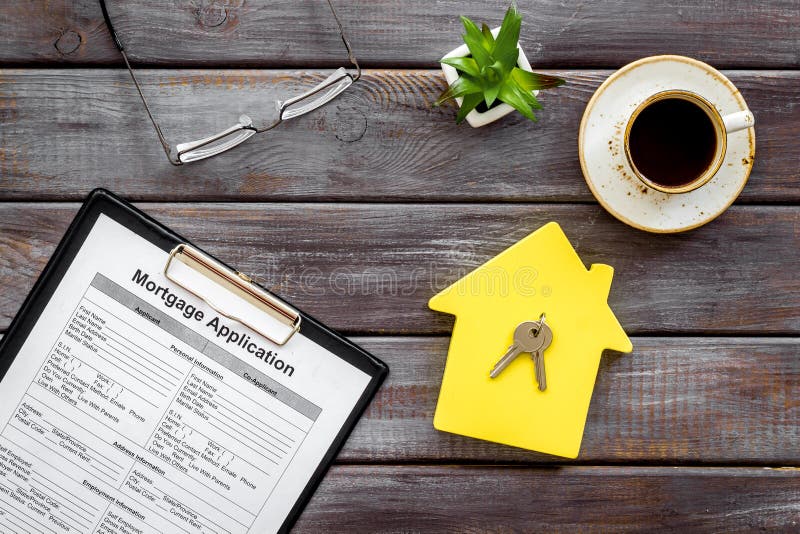 House mortgage with application, house toy, keys, glasses, coffee on wooden banker desk background top view