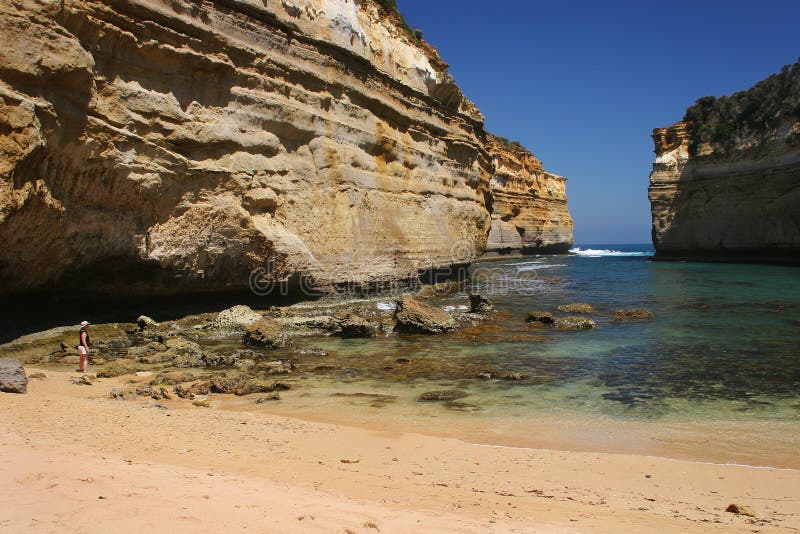 An elderly female tourist takes in the view from beach level of the surronding high cliff painted walls and beautiful clear water as the surf rolls into Loch Ard Gorge at Port Cambell National Park near the Great Ocean Road in Victoria, southern Australia. An elderly female tourist takes in the view from beach level of the surronding high cliff painted walls and beautiful clear water as the surf rolls into Loch Ard Gorge at Port Cambell National Park near the Great Ocean Road in Victoria, southern Australia.