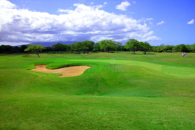 Wide shot of the ninth hole with rolling green hills and bunker against blue sky with white clouds. A great travel shot. Wide shot of the ninth hole with rolling green hills and bunker against blue sky with white clouds. A great travel shot.