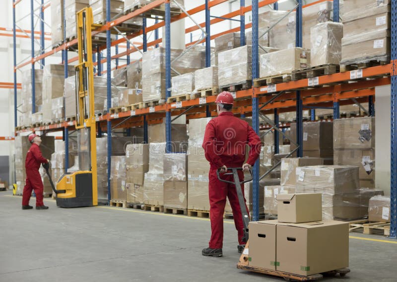 Two workers in uniforms and safety helmets working in storehouse. Two workers in uniforms and safety helmets working in storehouse