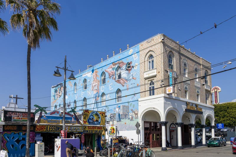 retail stores, surfing lessons and bike rentals and restaurants, a beautiful wall mural, tall green palm trees, people walking and blue sky in Venice California USA. retail stores, surfing lessons and bike rentals and restaurants, a beautiful wall mural, tall green palm trees, people walking and blue sky in Venice California USA