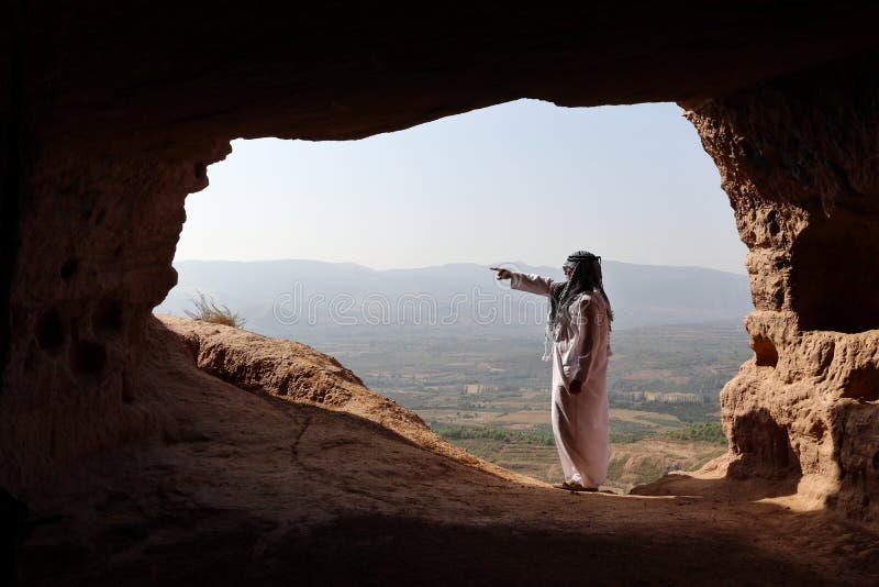 LOKALISIERTER ARABISCHER MANN IN EINER FERNhöhle MIT DJELLABA UND ARABISCHEM SCHAL UNTERSTREICHEND lizenzfreie stockfotografie