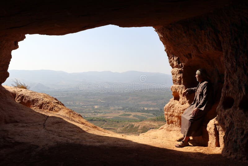 LOKALISIERTER EINSIEDLER-MANN MIT DJELLABA UND PALÄSTINENSISCHES SCHAL-SITZEN AM EINGANG EINER HÖHLE AUF DEM HOCH EINES BERGES stockfotos