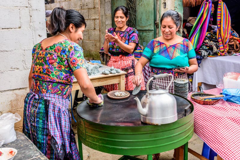 Santiago Sacatepequez, Guatemala - November 1, 2017: Local Maya women dressed in traditional clothing make corn tortillas in the street during the giant kite festival on All Saints Day. Santiago Sacatepequez, Guatemala - November 1, 2017: Local Maya women dressed in traditional clothing make corn tortillas in the street during the giant kite festival on All Saints Day.