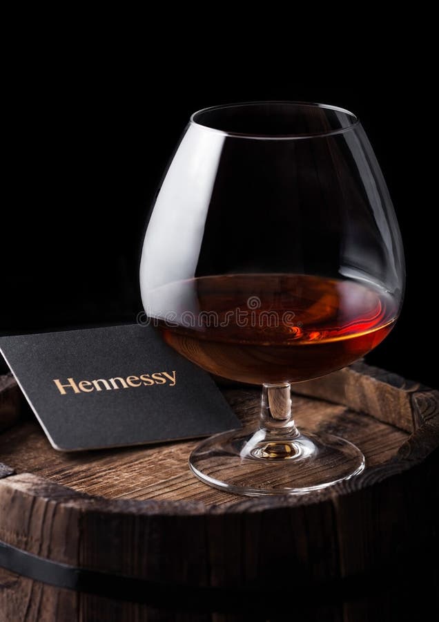 LONDON, UK - SEPTEMBER 04, 2018: Glass of Hennessy Cognac with original coaster on top of wooden barrel.