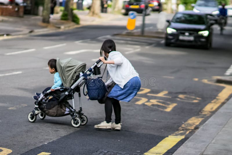 LONDON UK †”Maj 14, 2018: Kvinna med barnet i farligt läge, i att korsa den upptagna gatan arkivfoto LONDON UK †”Maj 14, 2018: Kvinna med barnet i farligt läge, i att korsa den upptagna gatan arkivfoto