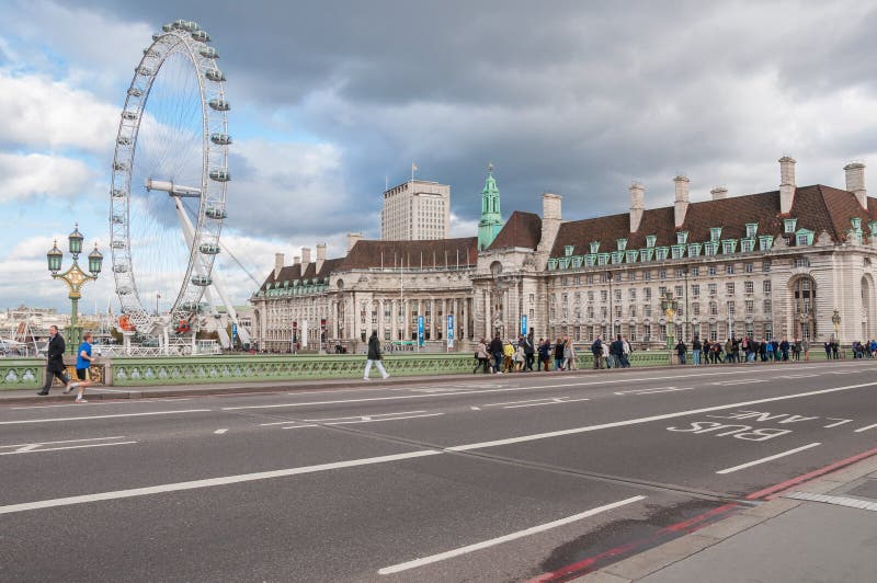 LONDON, UNITED KINGDOM - NOVEMBER 7, 2014: People cross the Westminster Bridge in front of the London Eye and County Hall, famous landmarks of London. LONDON, UNITED KINGDOM - NOVEMBER 7, 2014: People cross the Westminster Bridge in front of the London Eye and County Hall, famous landmarks of London.