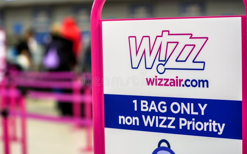 London, United Kingdom - February 05, 2019: Wizzair info table about maximum baggage size, blurred people at check in desks in background Wizz is Hungarian low cost operator founded in 2003. London, United Kingdom - February 05, 2019: Wizzair info table about maximum baggage size, blurred people at check in desks in background Wizz is Hungarian low cost operator founded in 2003.