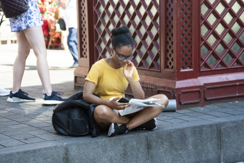 Londra, U K , 22 agosto 2019 - Lettura all'esterno Giovane donna afro-americana che guarda in basso, legge un libro nel libro fotografia stock libera da diritti Londra, U K , 22 agosto 2019 - Lettura all'esterno Giovane donna afro-americana che guarda in basso, legge un libro nel libro fotografia stock libera da diritti