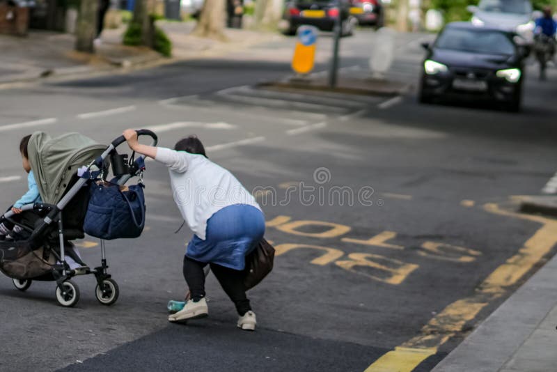 LONDRES, †BRITÁNICO “14 de mayo de 2018: Mujer con el niño en la situación peligrosa en calle muy transitada que cruza fotos de archivo LONDRES, †BRITÁNICO “14 de mayo de 2018: Mujer con el niño en la situación peligrosa en calle muy transitada que cruza fotos de archivo