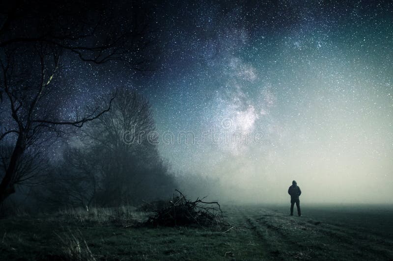 A lone hooded figure standing on a path on a spooky misty night, with a cold blue edit stock photography A lone hooded figure standing on a path on a spooky misty night, with a cold blue edit stock photography