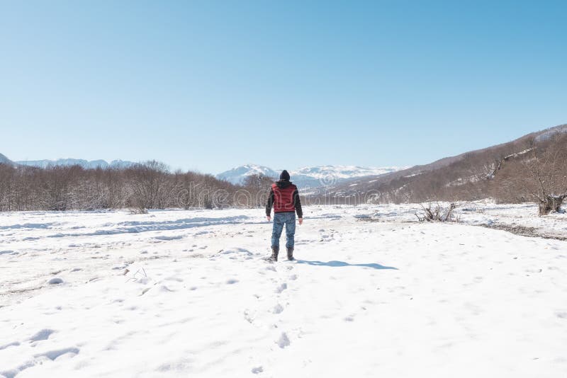 A Lone Man Walks Along the Frozen Bed of a Mountain River Stock Photo