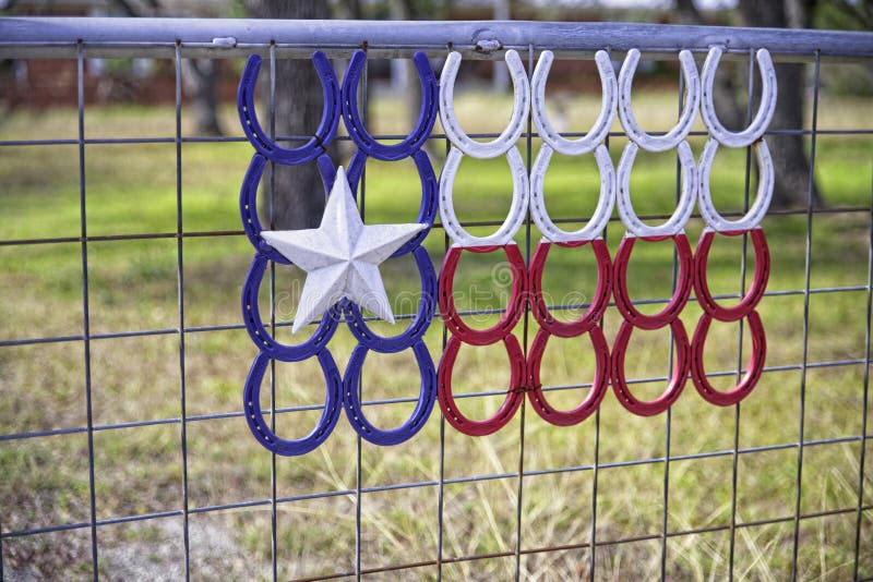 Lone Star Texas flag created with red, white, & blue horsehoes on gated fence.
