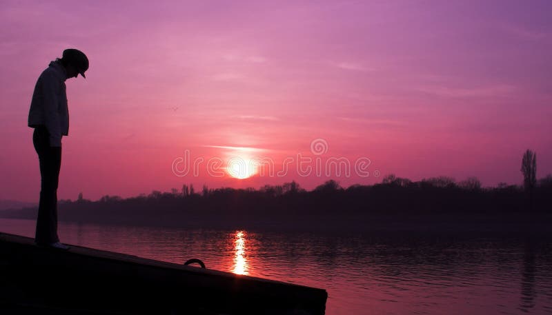 A silhouetted ženská postava stojí na neurčitý nabrezie v prednej časti purpurový západ slnka.