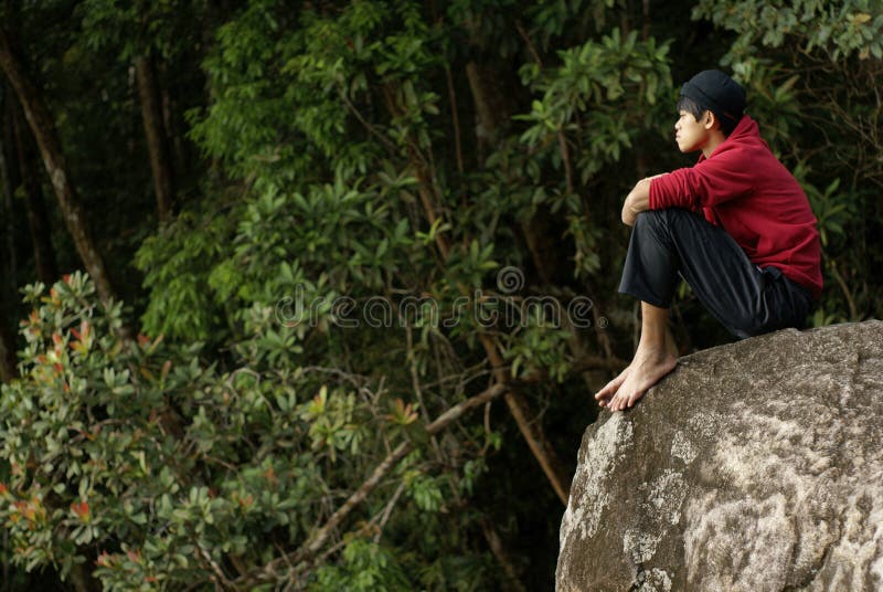 Lonely asian man sitting on rock