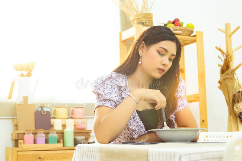 Lonely Asian woman sit at the table eating meal in the kitchen alone in the morning with beautiful sunshine light with copy space. royalty free stock photo Lonely Asian woman sit at the table eating meal in the kitchen alone in the morning with beautiful sunshine light with copy space. royalty free stock photo