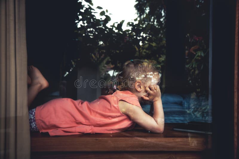 Lonely bored child girl in home isolation opposite window lying on windowsill royalty free stock photo