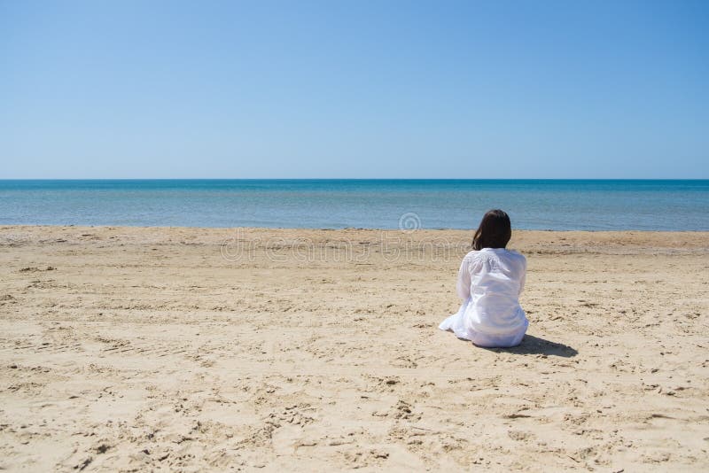 Lonely brunette woman with lobg hair on a beach and looking on sea. Back view.