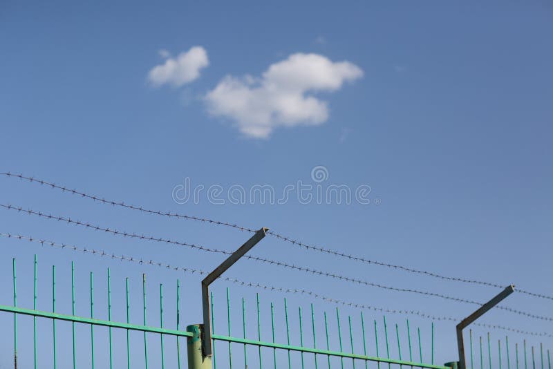 Lonely cloud in blue sky behind barbed wire. royalty free stock image