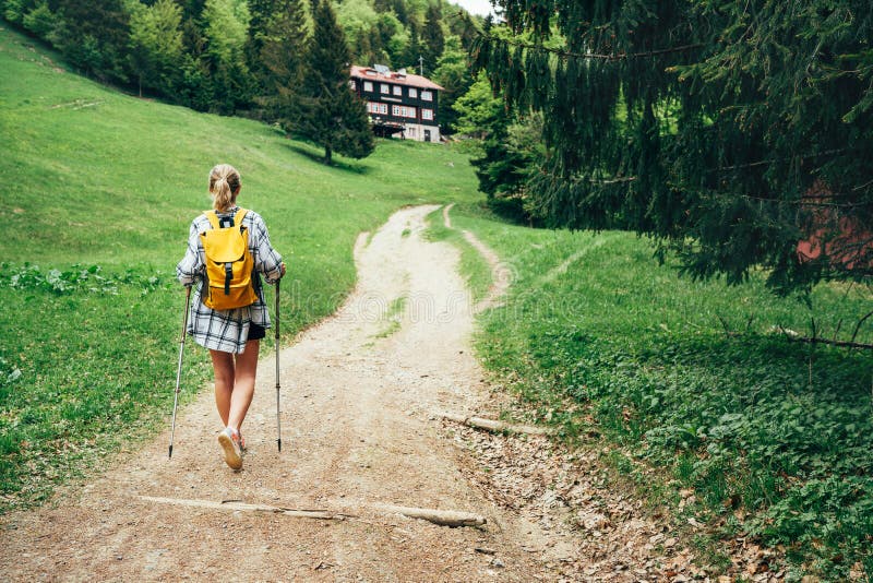 Osamelá žena so žltým ruksakom kráčajúca horským chodníkom s turistickými palicami k chate na slovensku, oblasť malá fatra