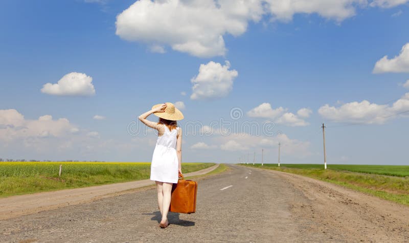 Lonely girl with suitcase at country road.