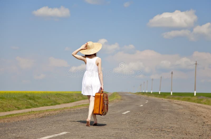 Lonely girl with suitcase at country road.