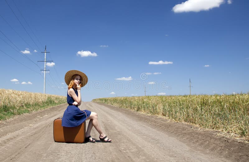 Lonely girl with suitcase at country road.