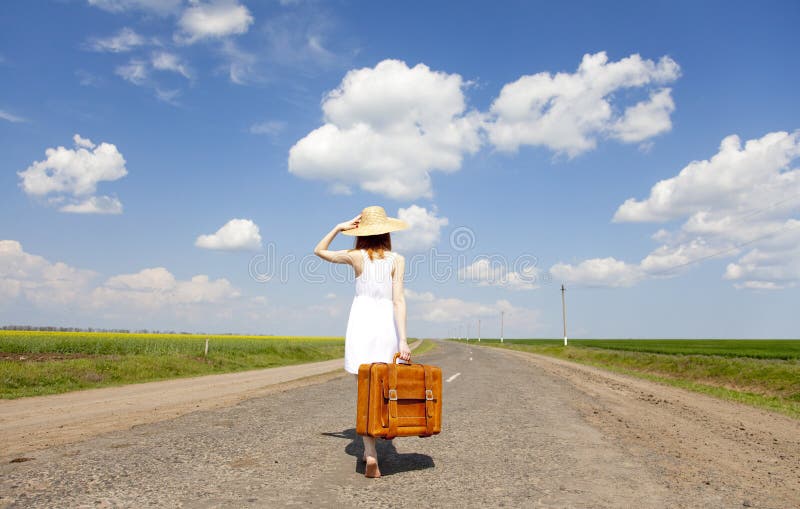 Lonely girl with suitcase at country road.