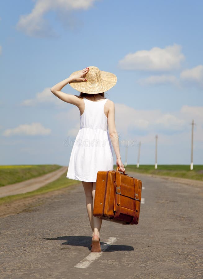 Lonely girl with suitcase at country road.