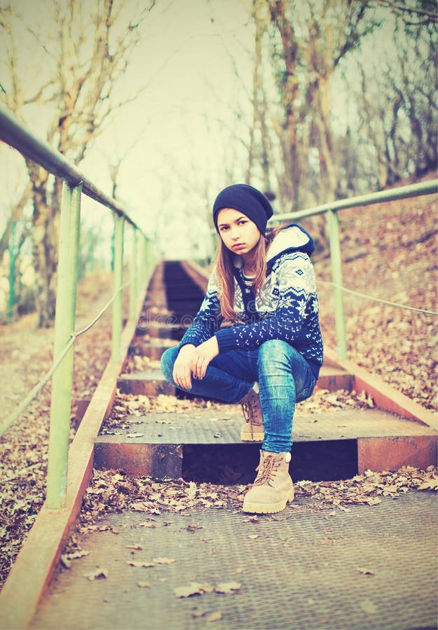 Lonely girl teenager in hat sitting on stairs and sad autumn