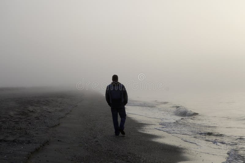 Uomo solo camminare su una spiaggia di nebbia.