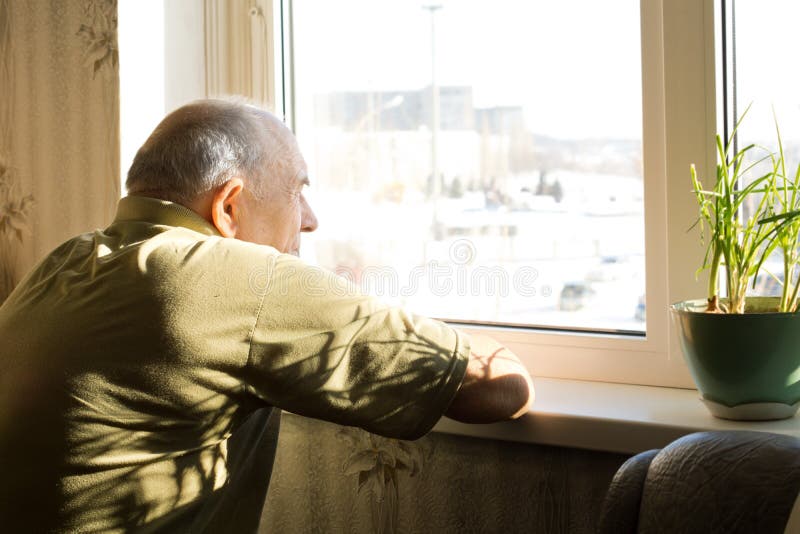 Lonely old man staring out of a window. Lonely old man in an old-age home staring out of a window as he longs for his freedom and friends royalty free stock photo