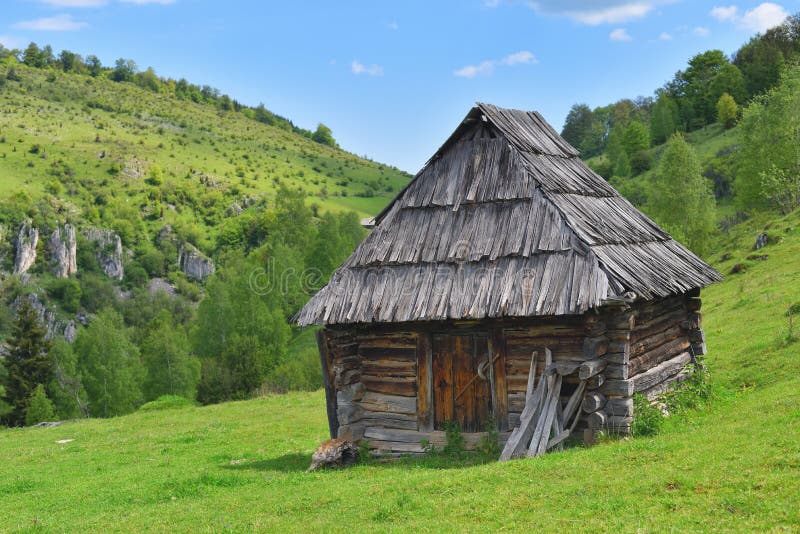 Lonely old wood house on a mountain hill with green grass against blue sky