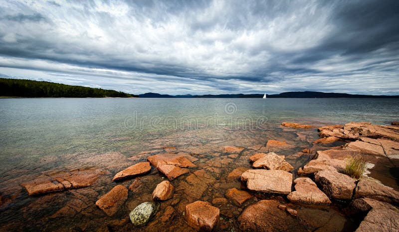 Lonely sail boat in archipelago. ramatic sky over stony beach coast and shallow water. Storsand, High Coast in northern Sweden